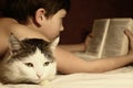 Teenager boy reading book in bed with sleeping cat Royalty Free Stock Photo