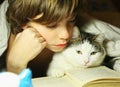 Teenager boy reading book with cat in bed Royalty Free Stock Photo