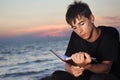 Teenager boy reads book sitting on beach