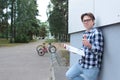 A teenager boy schoolchild or student is sitting on the stairs, reading a book, wearing glasses, in a shirt, smiling, a red back Royalty Free Stock Photo