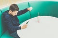 Teenager boy sits at cafe table, plays mobile games on smartphone. Boy is sitting with his hand up, victory, winnings. Royalty Free Stock Photo