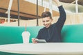 Teenager boy sits at cafe table, plays mobile games on smartphone. Boy is sitting with his hand up, victory, winnings. Royalty Free Stock Photo