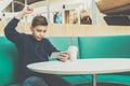 Teenager boy sits at cafe table, plays mobile games on smartphone. Boy is sitting with his hand up, victory, winnings. Royalty Free Stock Photo