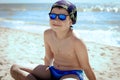 A teenager boy sitting on the sand in swimming trunks, blue sun glasses, is engaged in meditation, relaxation and yoga on the sea Royalty Free Stock Photo