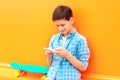 teenager boy uses smartphone, skateboard on a colorful orange Royalty Free Stock Photo