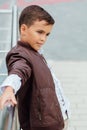 Teenager boy is waiting for the stairs at the railing. Fashionable kid in stylish city clothes.