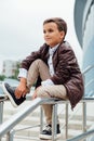 Teenager boy is waiting for the stairs at the railing. Fashionable kid in stylish city clothes.