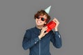 Celebration Concept. Teenager boy in birthday cap and sunglasses standing isolated on grey shaking present smiling Royalty Free Stock Photo