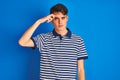 Teenager boy wearing casual t-shirt standing over blue isolated background pointing unhappy to pimple on forehead, ugly infection Royalty Free Stock Photo