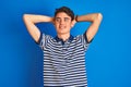 Teenager boy wearing casual t-shirt standing over blue isolated background relaxing and stretching, arms and hands behind head and Royalty Free Stock Photo