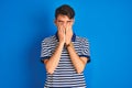 Teenager boy wearing casual t-shirt standing over blue isolated background rubbing eyes for fatigue and headache, sleepy and tired