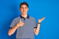 Teenager boy wearing casual t-shirt standing over blue isolated background Showing palm hand and doing ok gesture with thumbs up, Royalty Free Stock Photo