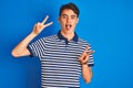 Teenager boy wearing casual t-shirt standing over blue isolated background smiling with tongue out showing fingers of both hands Royalty Free Stock Photo