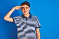 Teenager boy wearing casual t-shirt standing over blue isolated background very happy and smiling looking far away with hand over Royalty Free Stock Photo