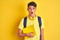 Teenager boy wearing headphones and backpack reading a book over isolated background scared in shock with a surprise face, afraid Royalty Free Stock Photo