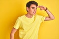 Teenager boy wearing yellow t-shirt over isolated background very happy and smiling looking far away with hand over head Royalty Free Stock Photo