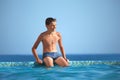 Teenager boy wets feet water in pool against sea