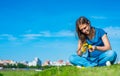 Teenager brunette girl with long hair sit on the grass and wreathes a wreath of yellow dandelion flowers on sky background with co