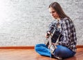 Teenager brunette girl with long hair sitting on the floor and playing an black acoustic guitar on gray wall background Royalty Free Stock Photo