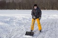 Teenager brush snow with shovel on ice of forest lake for ice skating. Healthy lifestyle