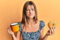 Teenager caucasian girl eating doughnut and drinking coffee puffing cheeks with funny face Royalty Free Stock Photo