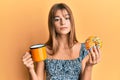 Teenager caucasian girl eating doughnut and drinking coffee relaxed with serious expression on face Royalty Free Stock Photo