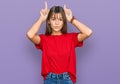 Teenager caucasian girl wearing casual red t shirt doing funny gesture with finger over head as bull horns