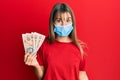 Teenager caucasian girl wearing medical mask holding 10 united kingdom pounds banknotes scared and amazed with open mouth for