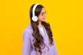 Teenager child girl in headphones listening music, wearing stylish casual outfit isolated over yellow background. Royalty Free Stock Photo