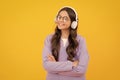 Teenager child girl in headphones listening music, wearing stylish casual outfit isolated over yellow background. Royalty Free Stock Photo