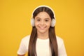 Teenager child girl in headphones listening music, wearing stylish casual outfit isolated over yellow background. Happy Royalty Free Stock Photo