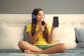 Teenager child girl wearing headphones listening music on smart phone sitting on bed in her room. Happy teen girl Royalty Free Stock Photo