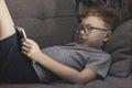 A boy with glasses for vision lies on the couch and looks into the tablet Royalty Free Stock Photo