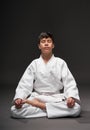 A teenager dressed in martial arts clothing meditating on a dark gray background, a sports concept Royalty Free Stock Photo