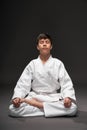 A teenager dressed in martial arts clothing meditating on a dark gray background, a sports concept Royalty Free Stock Photo