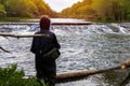 Teenager fishing with a rod in the middle of a river with a small waterfall of water branches and logs washed away by the flood in Royalty Free Stock Photo