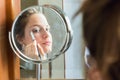 Teenager girl looking her self in a round mirror applying eyeshadow with a brush. Royalty Free Stock Photo