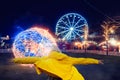 Teenager girl back to camera. Hands up in the air, Her jacket if lifted by a strong wind. Illuminated fun fair park out of focus