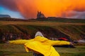 Teenager girl back to camera. Hands up in the air, Her jacket if lifted by a strong wind. Sunset sky and castle in the background