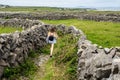 Teenager girl with backpack on a warm sunny day walking on footpath between stone fences. Inishmore, Aran Islands, County Galway,