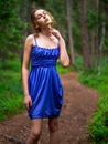 Teenager girl in a blue high fashion dress posing on a footpath in a forest. Senior prom pictures. Glamour and elegance concept.