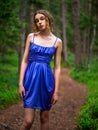 Teenager girl in a blue high fashion dress posing on a footpath in a forest. Senior prom pictures. Glamour and elegance concept.