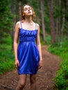 Teenager girl in a blue high fashion dress posing on a footpath in a forest. Senior prom pictures. Glamour and elegance concept.