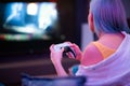 Teenager girl with colorful blue and pink hair hold joystick and play video games at home at night.