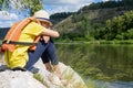 Teenager girl dreams sitting on a stone shore. girl sitting in a life jacket near the water, river Royalty Free Stock Photo