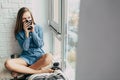 Teenager girl drinking coffee from black cuÃâ¬.young woman sitting on window sill in shirt,looking thoughtfully,watch out the windo Royalty Free Stock Photo