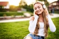 Teenager girl enjoying life and sitting in the grass in a public park, while listening to music with headphones on her head with Royalty Free Stock Photo