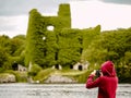 Teenager girl filming on her smart phone old castle and a river, Menlo castle, Galway, Irleland. Concept: modern technology used