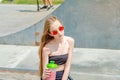 Teenager girl with a fitness cup sits on a bench near the skate track in summer. Outdoor activity, skiing Royalty Free Stock Photo