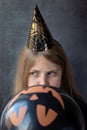 A teenager girl in a Halloween paper cap inflating black ball for Halloween. People, Halloween, decoration concept
